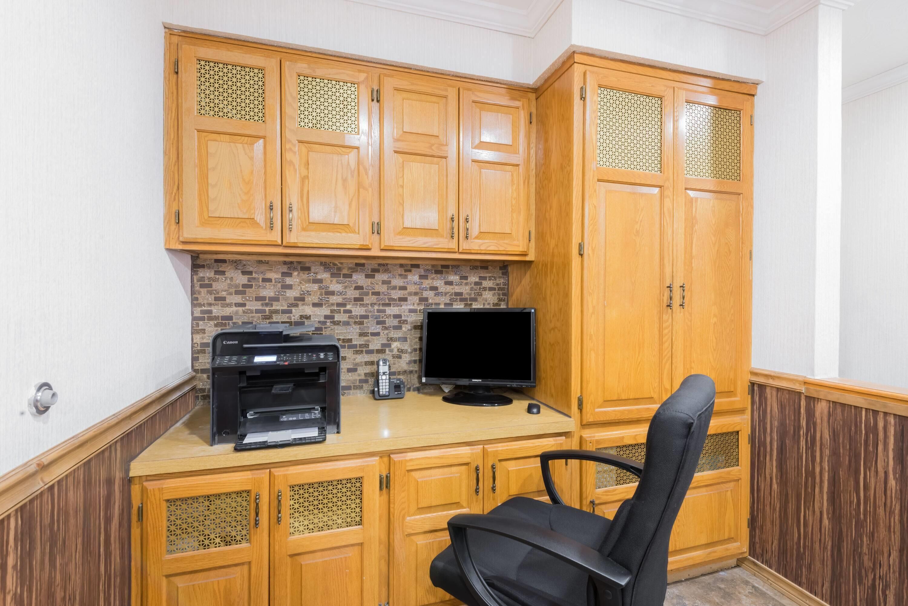 A small office space with wooden cabinets, a printer, a monitor, and a black office chair.