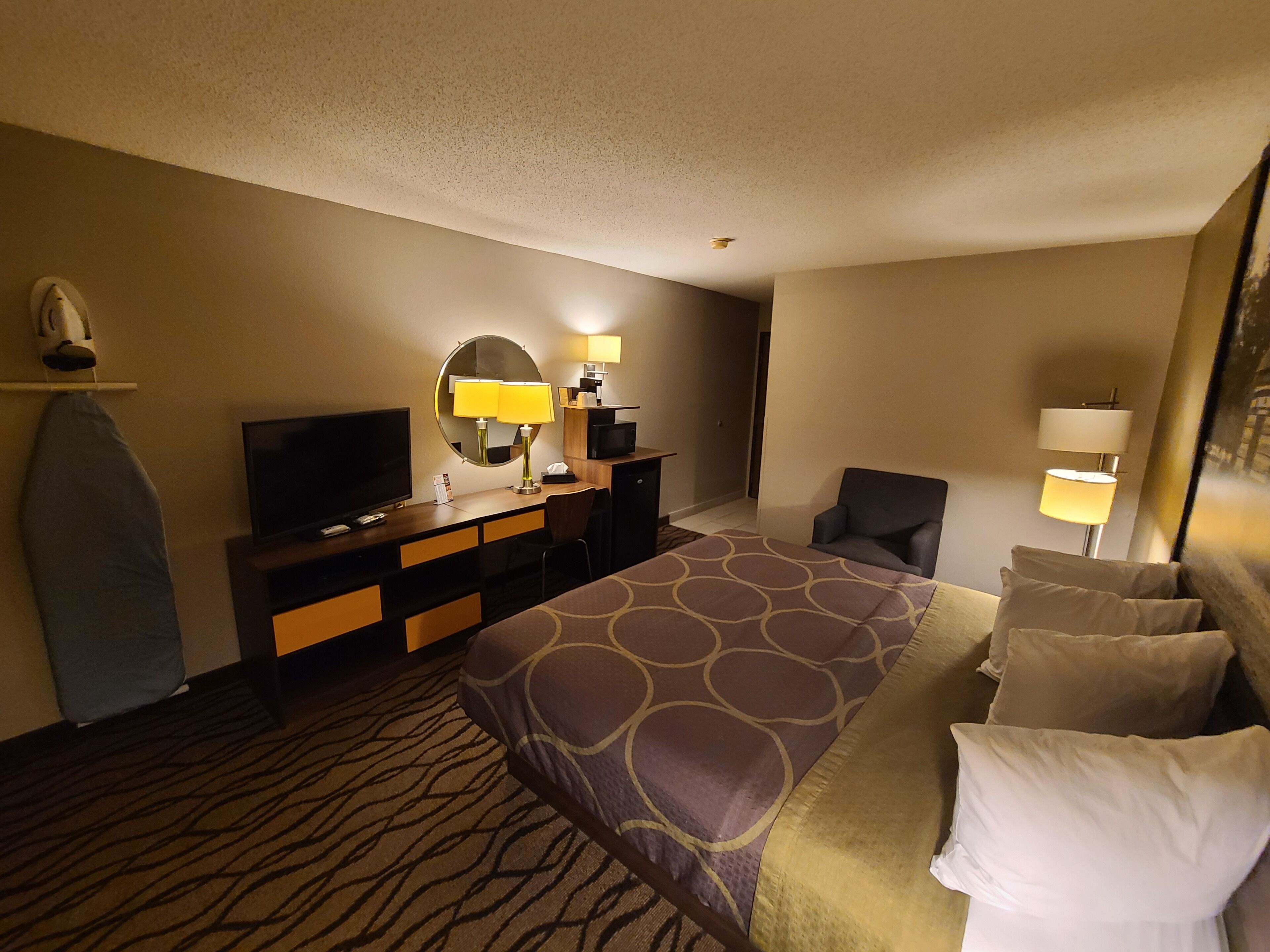 A hotel room with a bed, a TV, a desk with a lamp, a chair, and a large mirror.