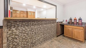 A kitchen with a brick backsplash, wooden cabinets, and a countertop with various items. - Super 8 by Wyndham Bedford (Bedford)
