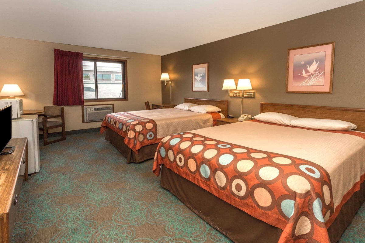 A hotel room with two beds, a desk, a chair, and a window with curtains.