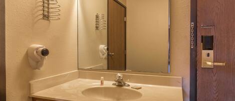 A bathroom with a sink, mirror, towel dispenser, and a security camera.