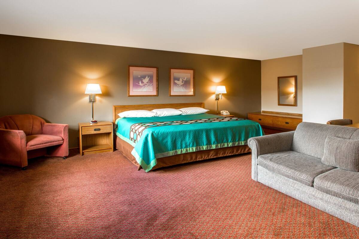 A hotel room with a bed, two bedside lamps, a chair, a sofa, and a nightstand with a phone.