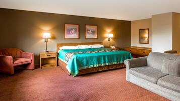 A hotel room with a bed, two bedside lamps, a chair, a sofa, and a nightstand with a phone.