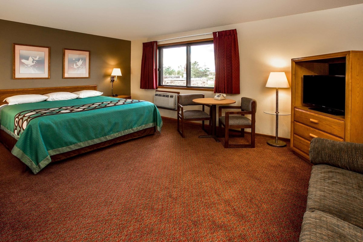 A hotel room with a bed, a desk, a chair, a television, and a sofa.