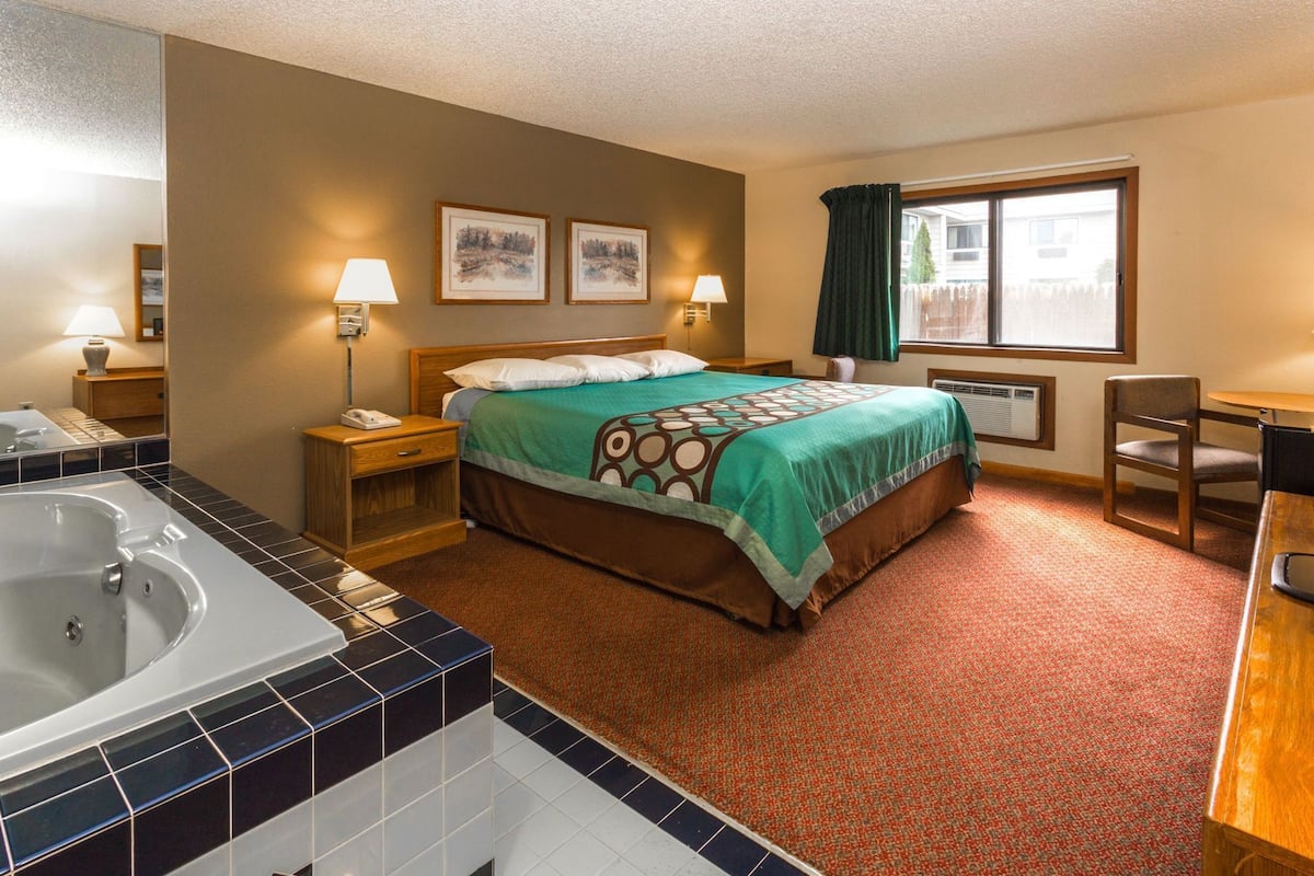A hotel room with a bed, a desk, a chair, a bathroom with a bathtub, and two wall-mounted lamps.