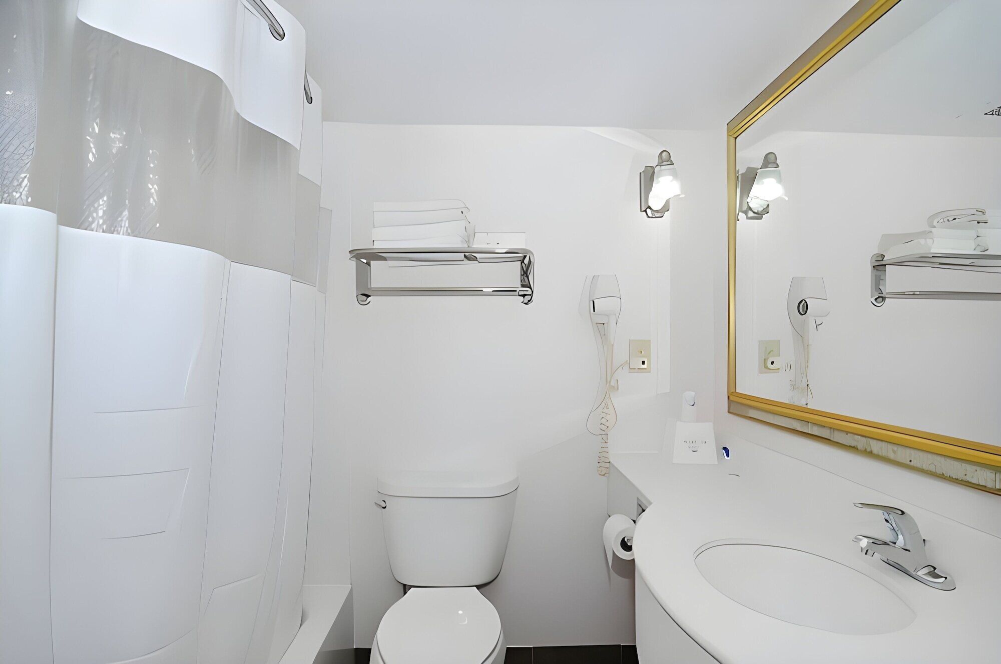 Un baño moderno con inodoro, lavamanos y espejo. Hay un perchero sobre el inodoro y una toalla colgada en él. El baño presenta una decoración en blanco.