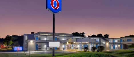 Un motel con un llamativo letrero con el número '6', un edificio moderno con varias unidades y una entrada bien iluminada.