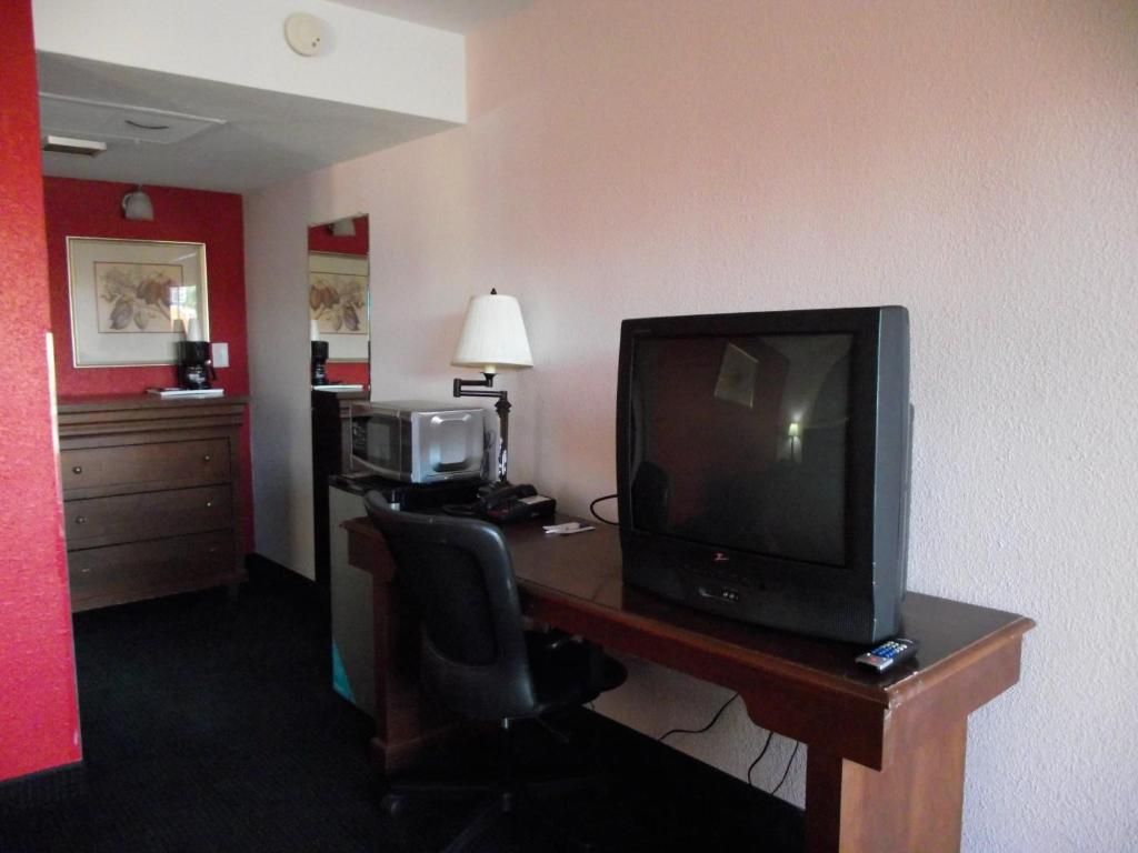 Habitación de hotel con escritorio, televisión, silla, lámpara, microondas y cafetera.