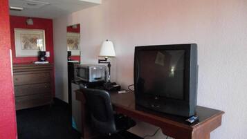 Habitación de hotel con escritorio, televisión, silla, lámpara, microondas y cafetera.