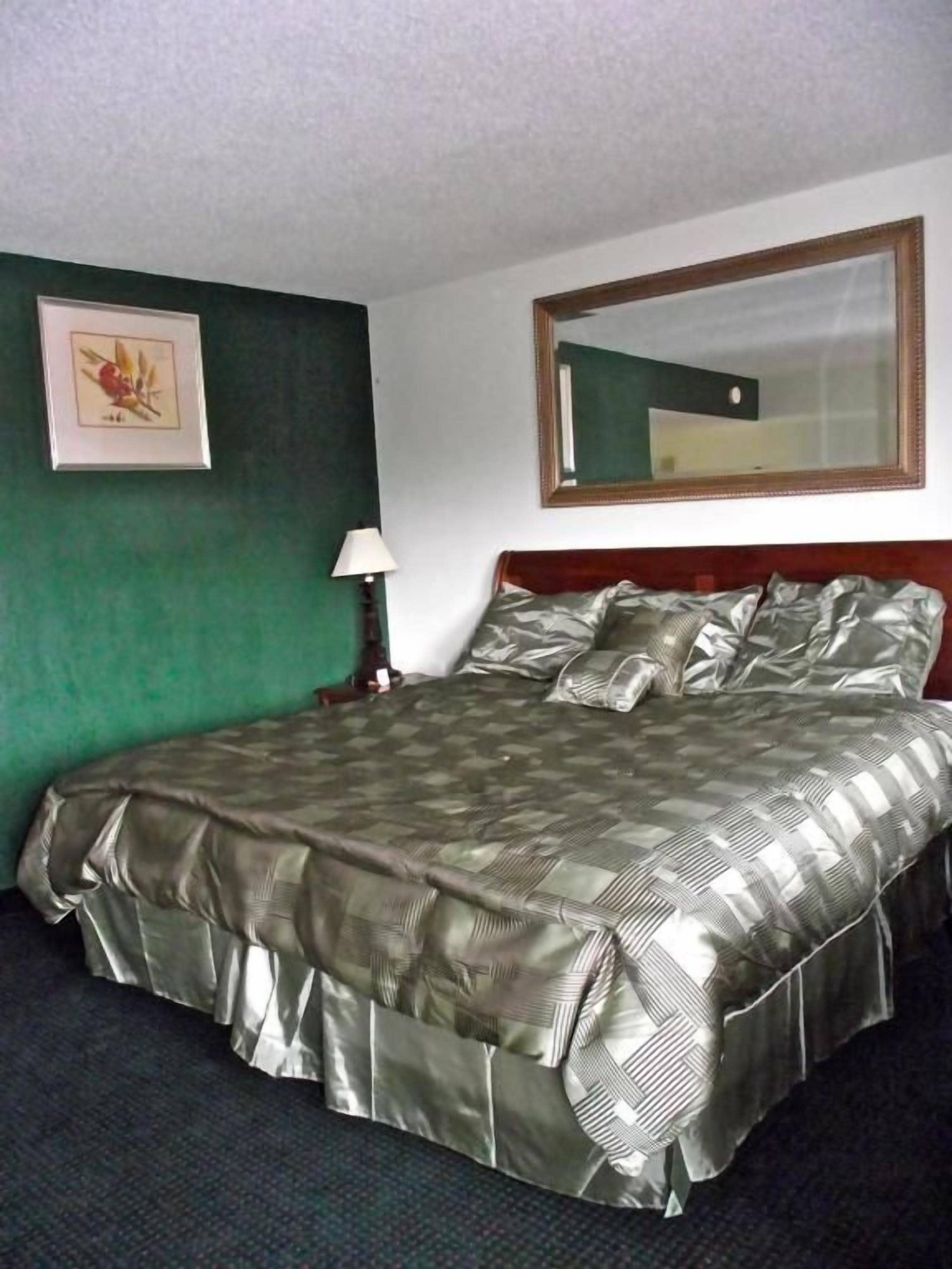 A standard hotel room with a bed, a nightstand, a lamp, a framed picture on the wall, and a mirror above the bed.