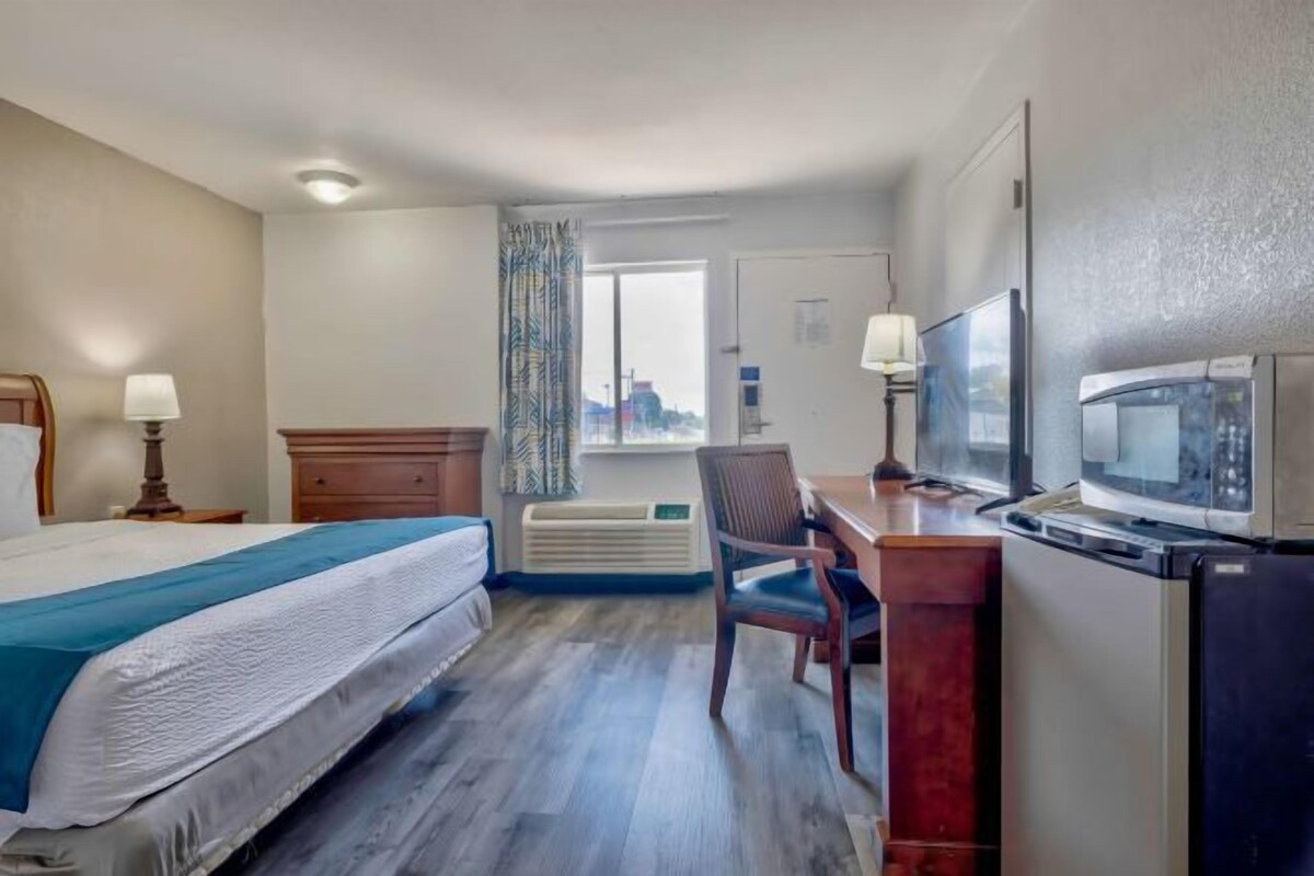 A hotel room with a bed, desk, chair, TV, and air conditioning unit.