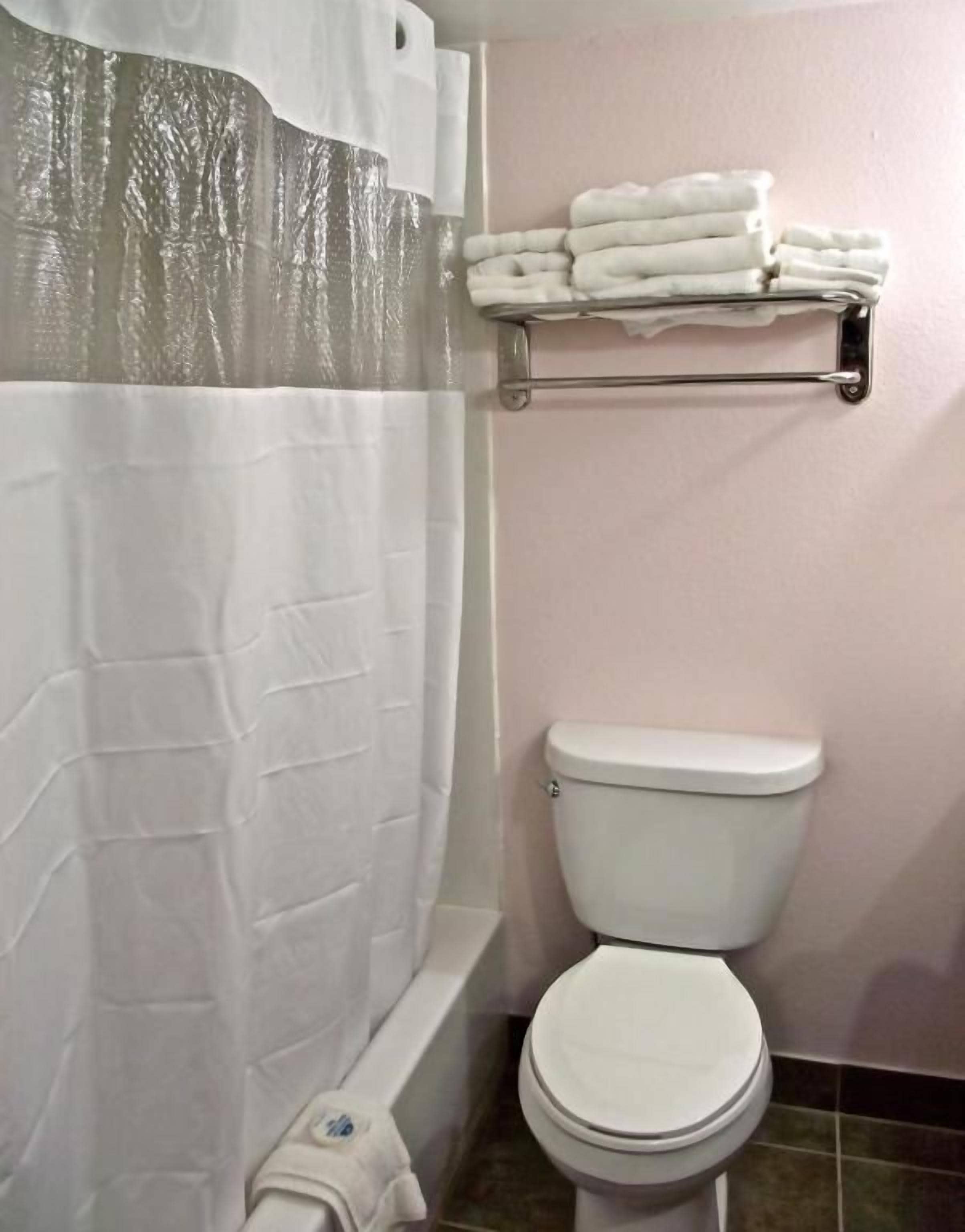 A bathroom with a white toilet, a shower curtain, and a towel rack with folded towels.