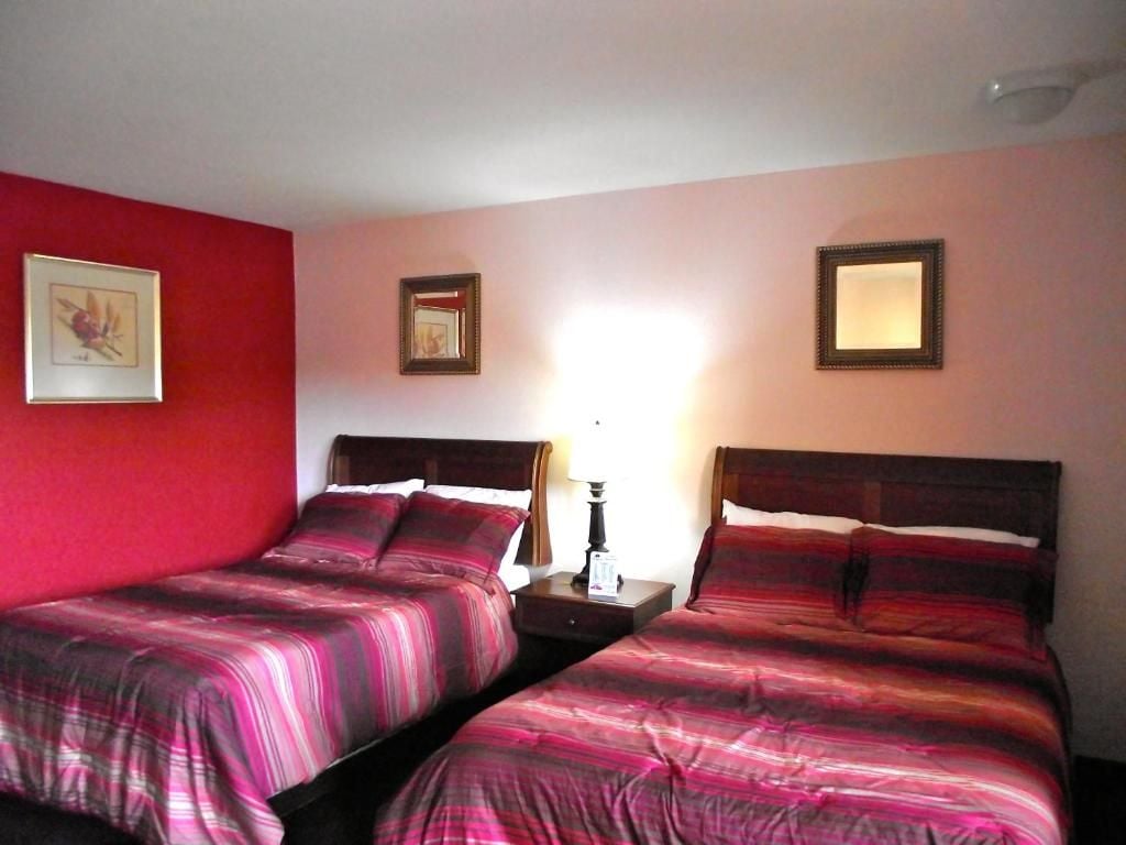 A hotel room with two beds, a nightstand, and a wall-mounted lamp.