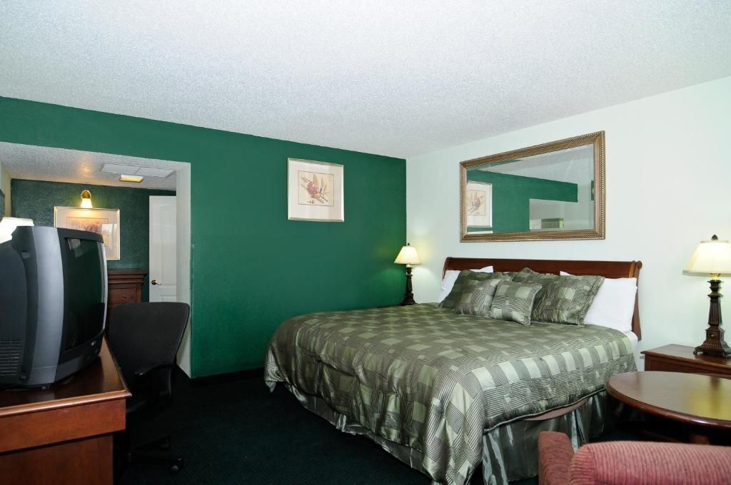 A hotel room with a bed, two bedside lamps, a desk with a television, and a chair.