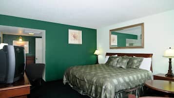 A hotel room with a bed, two bedside lamps, a desk with a television, and a chair.