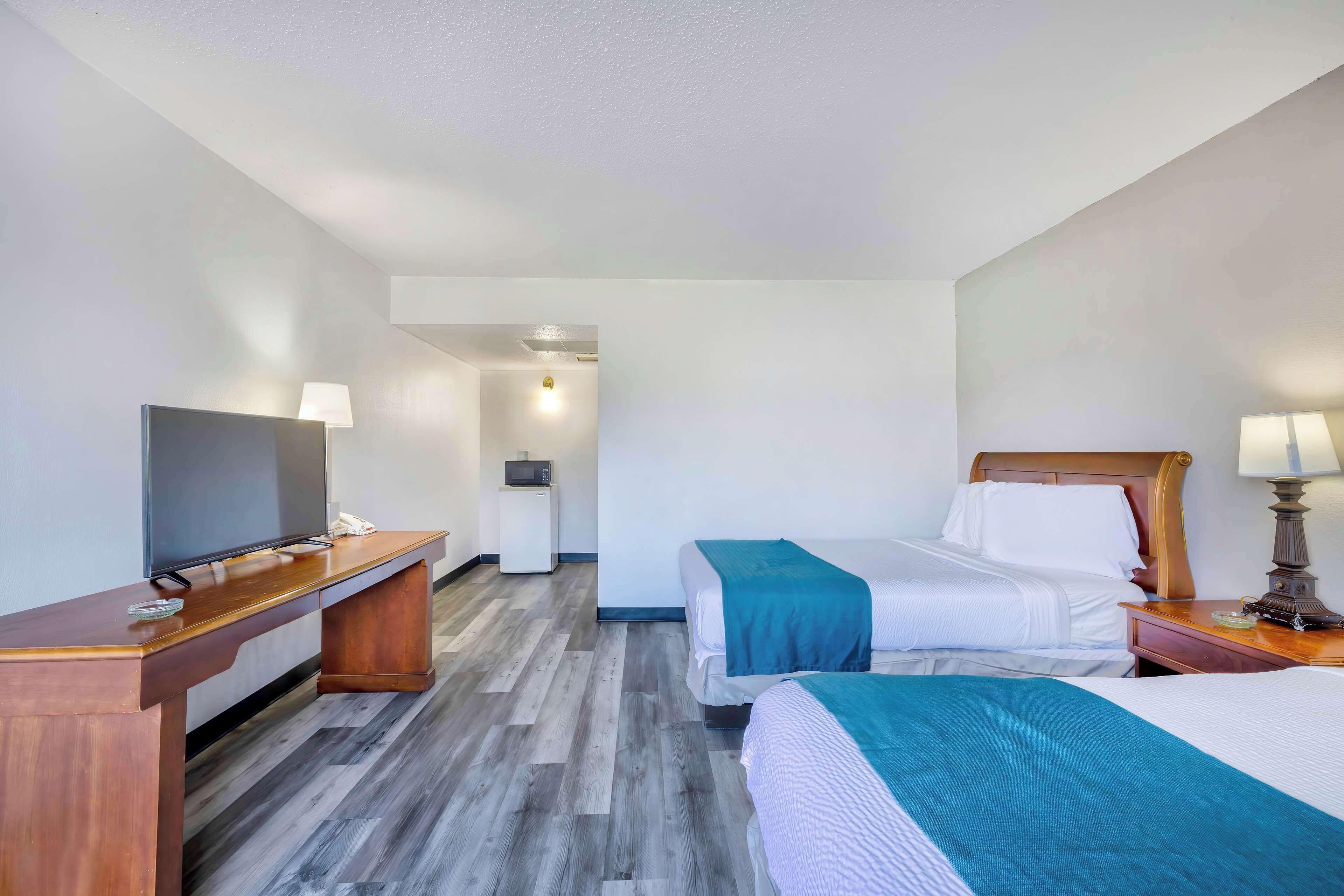 A hotel room with two beds, a desk with a television, and a small kitchenette.