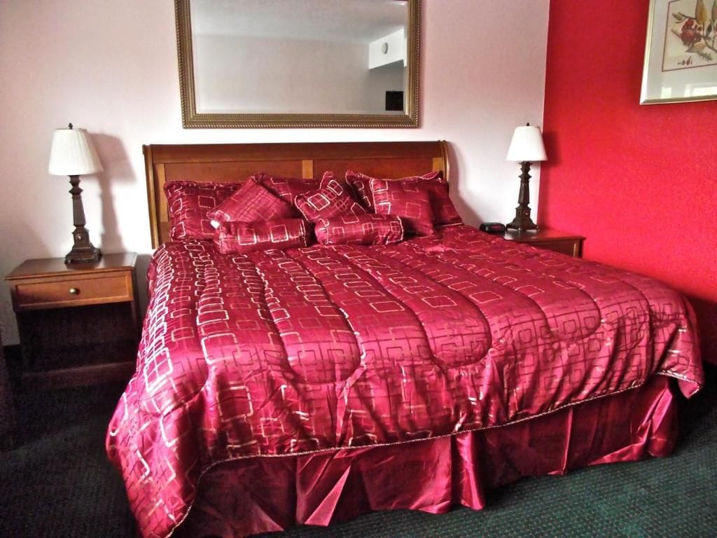 Habitación de hotel con una cama grande, dos mesitas de noche con lámparas, un espejo en la pared y un cuadro enmarcado.