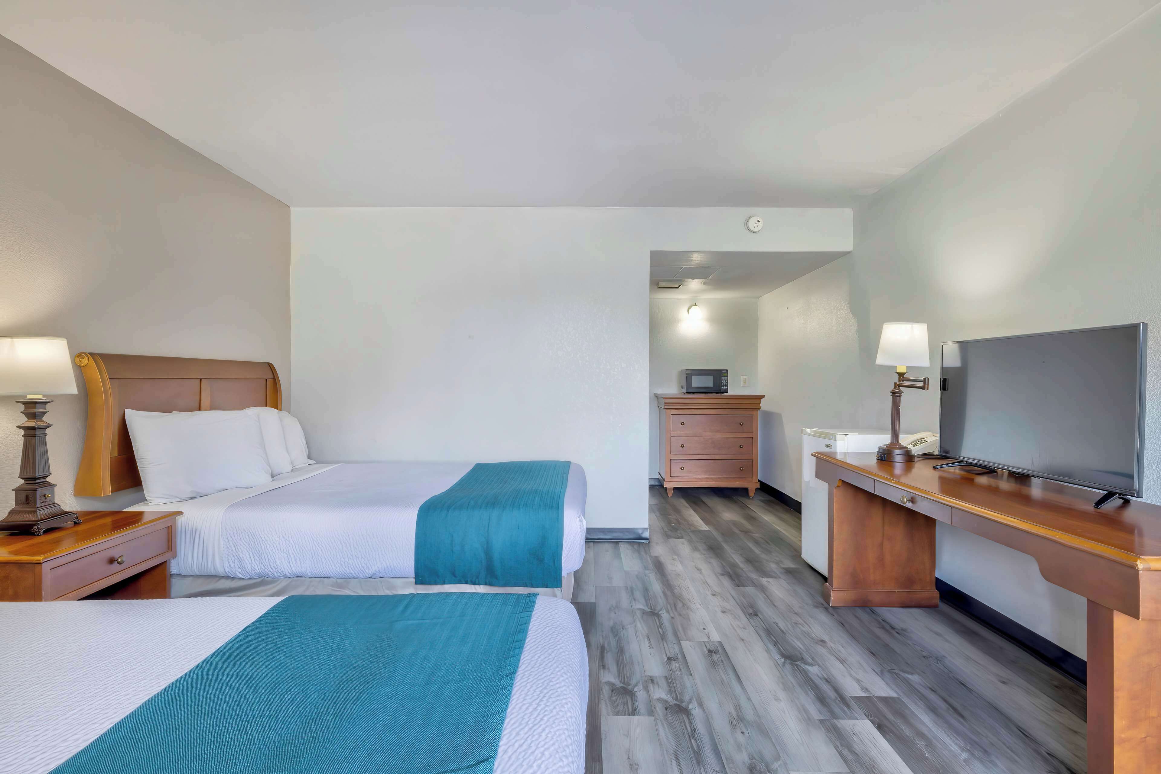 A hotel room with two beds, a desk with a TV, a dresser, and a lamp.