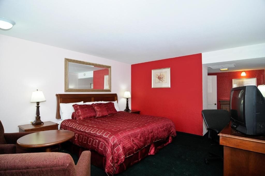 A hotel room with a bed, a desk with a television, a chair, and a lamp.