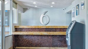 A reception area with a large number '6' on the wall, a tiled mosaic wall, a reception desk, and a wall-mounted security camera. - Motel 6 - Harrisburg, PA - Near PA Expo Center  (Harrisburg)