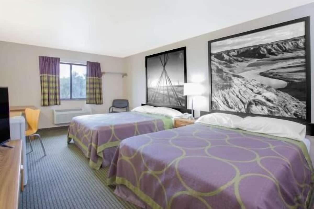 A hotel room with two beds, a desk, a chair, a window with curtains, and a large black and white landscape painting on the wall.