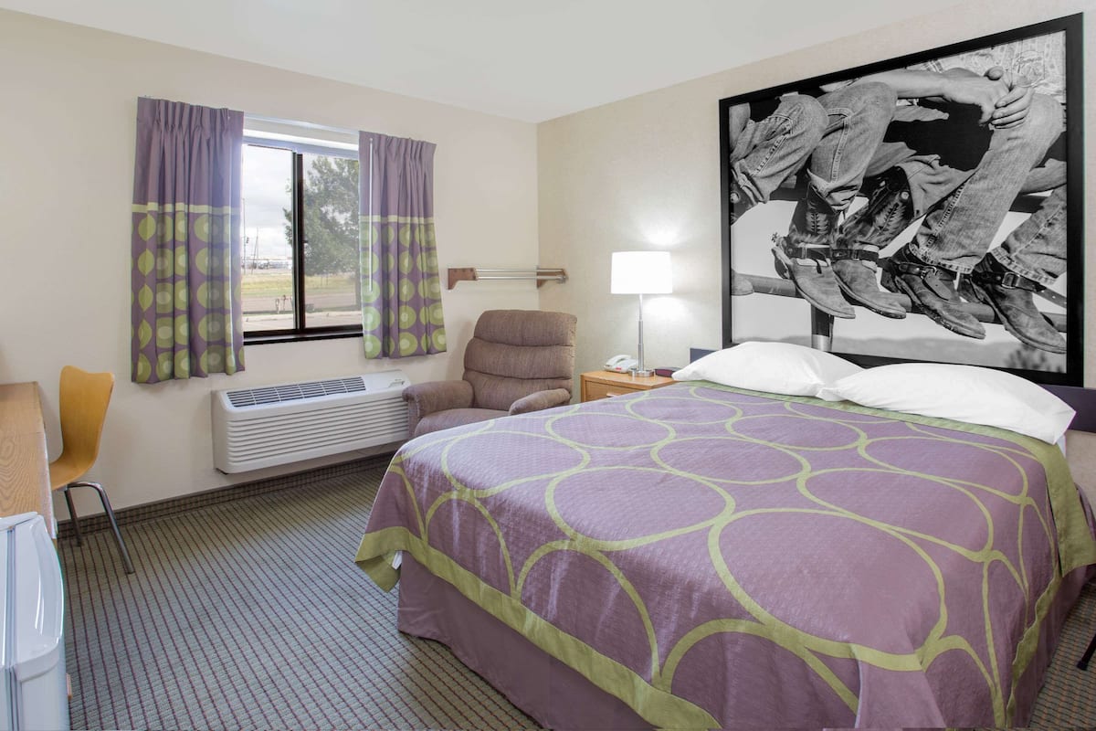 A hotel room with a bed, a chair, a desk, a lamp, and a window with curtains.
