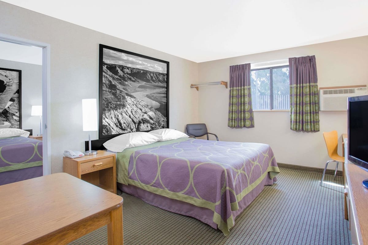 A hotel room with a bed, a desk, a chair, a television, and a window with curtains.