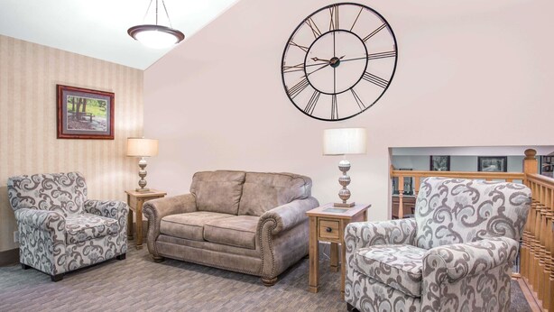 A living room with patterned armchairs, a sofa, a large wall clock, and a framed picture on the wall. - Super 8 by Wyndham Havre (Havre)
