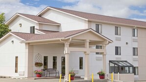 A modern hotel with a covered entrance, potted plants, and a clear sky. - Super 8 by Wyndham Havre (Havre)