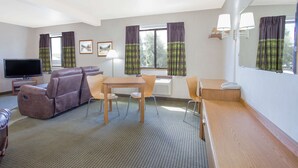 A hotel room with a sofa, a TV, a dining table with chairs, a small kitchen area, and a large window with curtains. - Super 8 by Wyndham Havre (Havre)