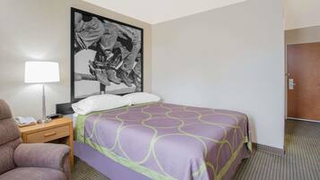 Ein Hotelzimmer mit Bett, Sessel, Nachttisch mit Lampe und Tür.