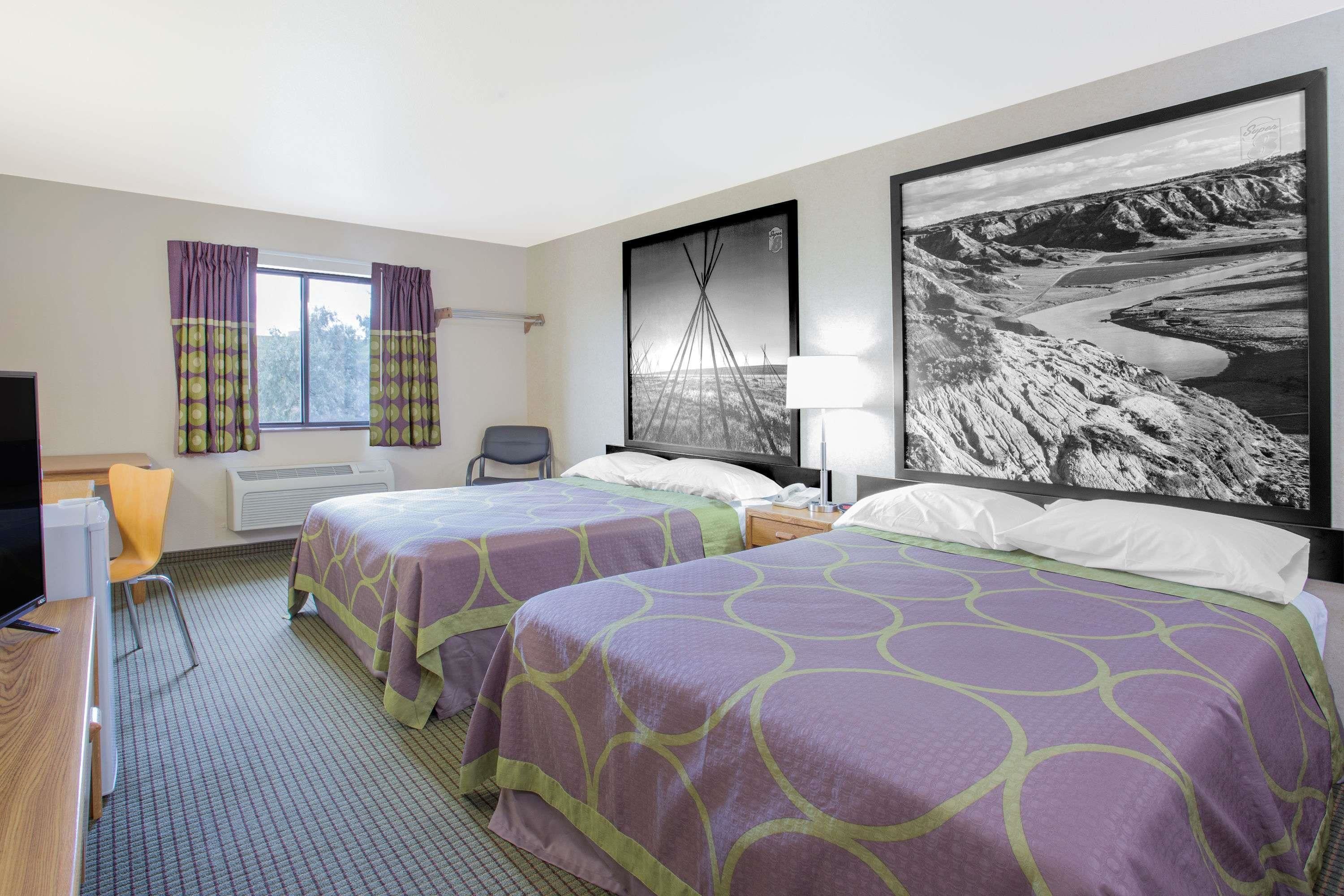 Une chambre d’hôtel avec deux lits, un bureau, une chaise, un téléviseur et une grande photographie en noir et blanc accrochée au mur.