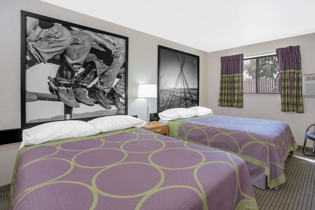 A hotel room with two beds, a large framed black and white photograph on the wall, a window with curtains, and a chair.