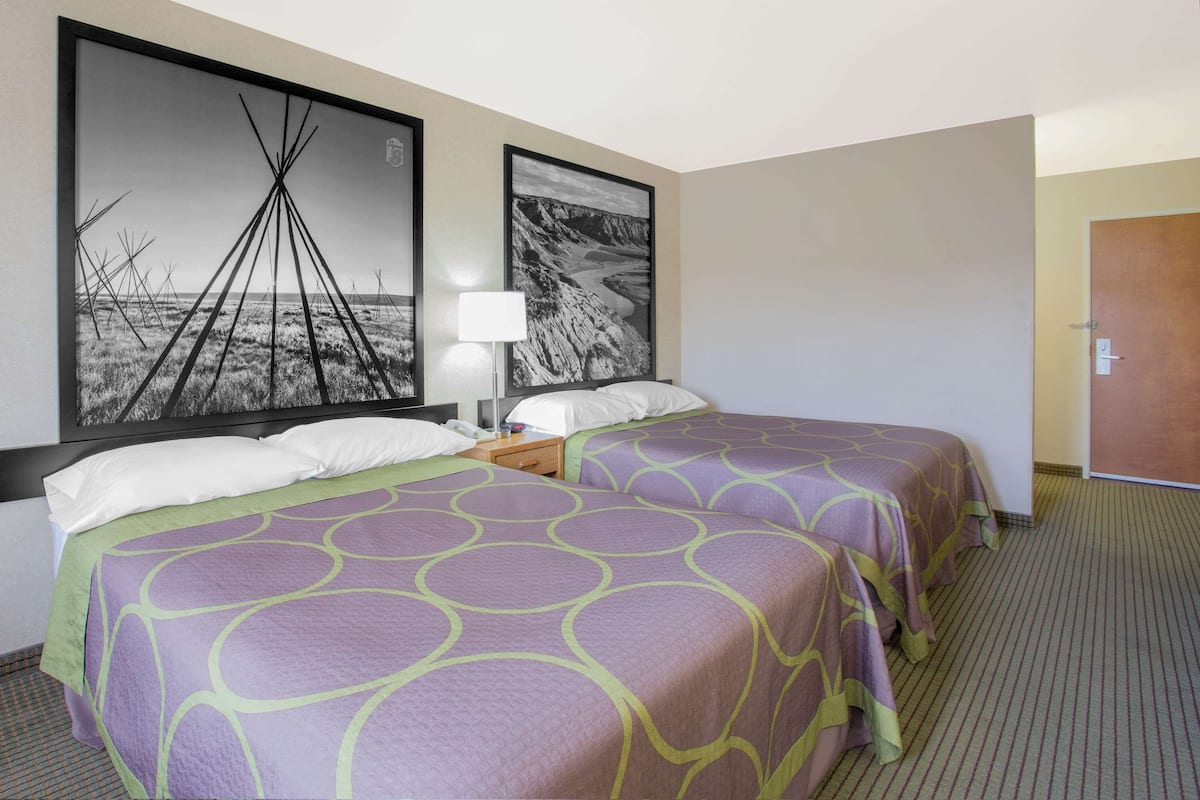 A hotel room with two beds, a nightstand, a lamp, and two large framed pictures on the wall.