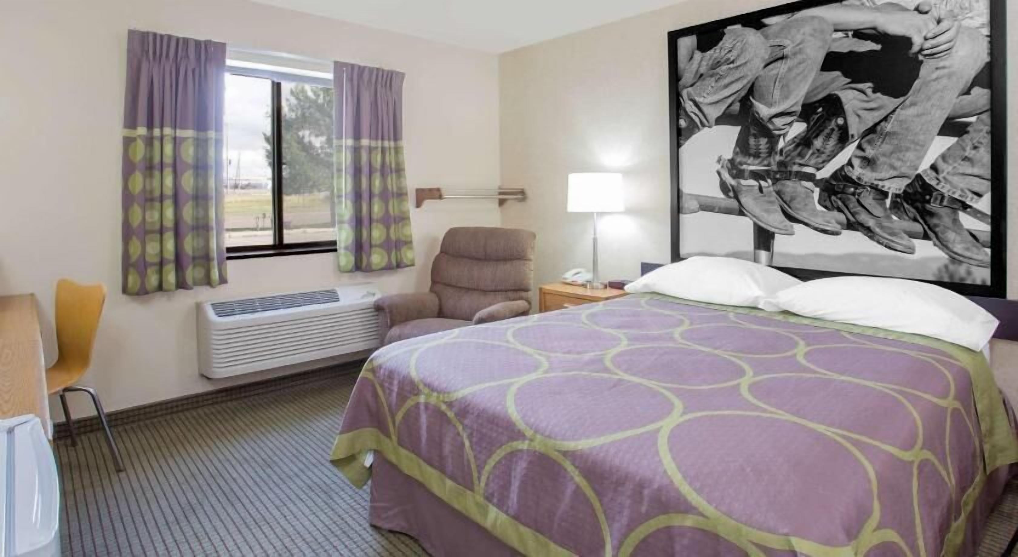 Une chambre d’hôtel comprenant un lit, une chaise, un bureau, une lampe, une fenêtre avec des rideaux et un climatiseur fixé au mur.