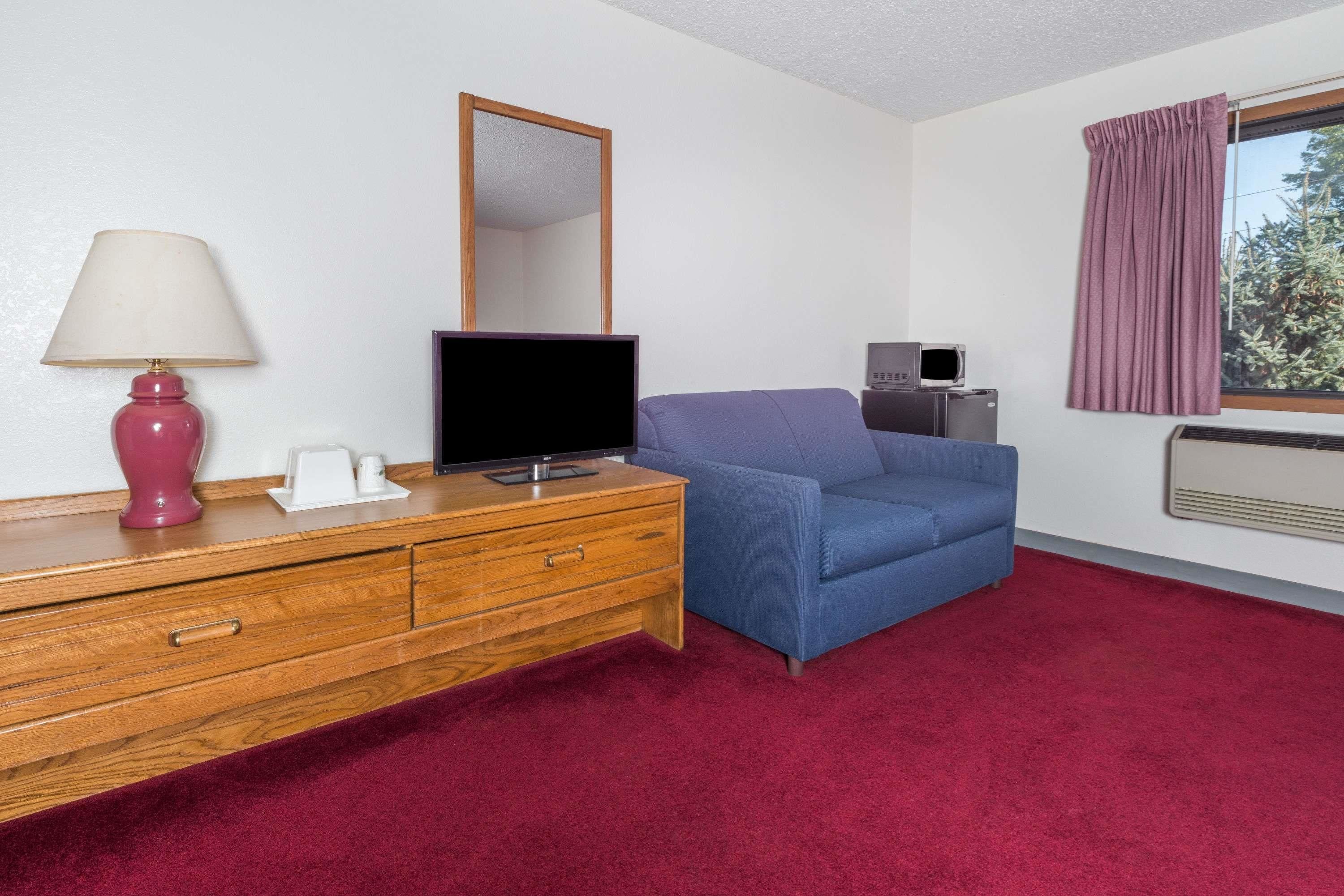 Ein Hotelzimmer mit einem hölzernen Schminktisch, einem Fernseher, einem blauen Sofa, einem Spiegel, einem Fenster mit violetten Vorhängen und einem roten Teppich.