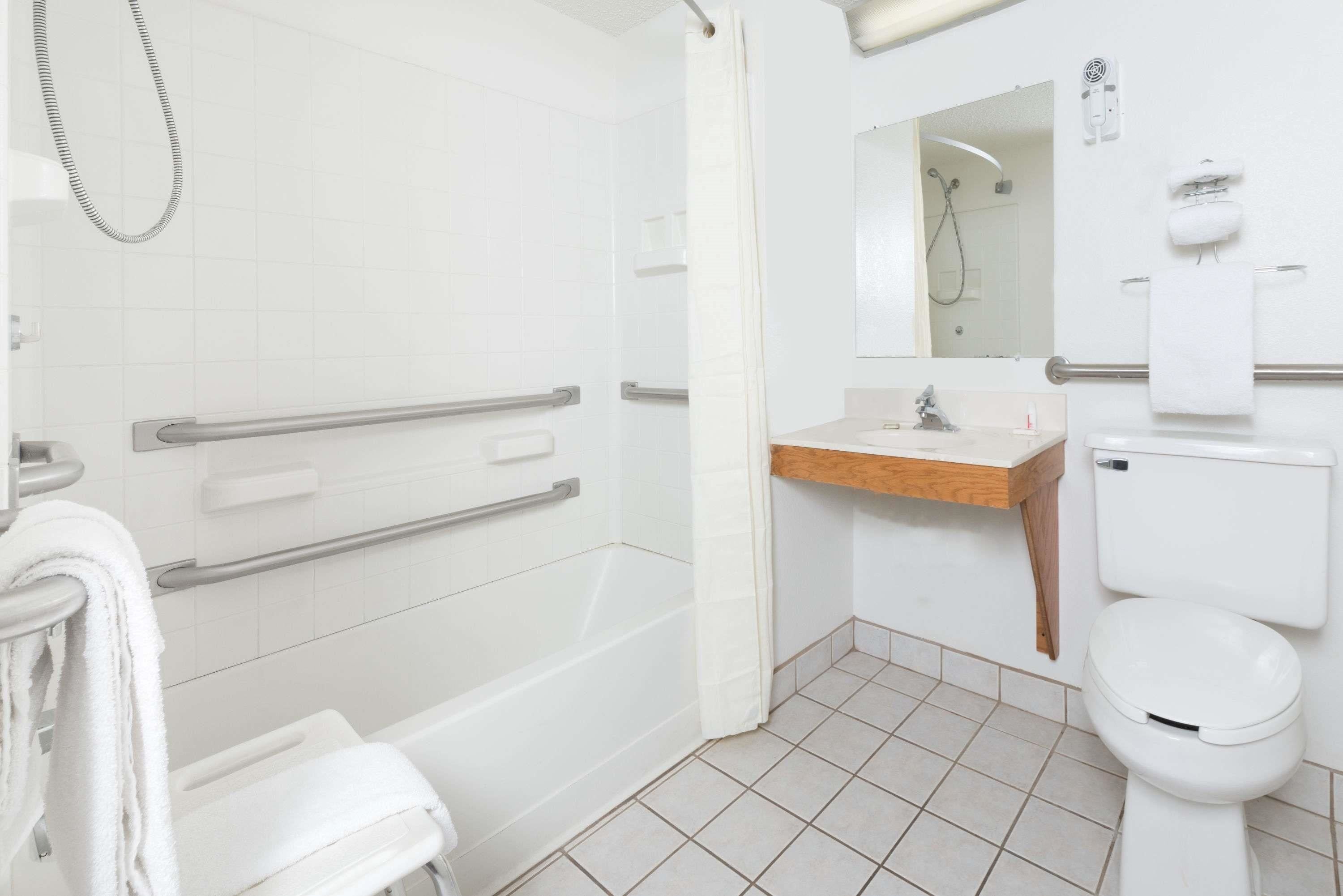 A modern bathroom with a shower, toilet, and sink. It includes grab bars and a towel rack.