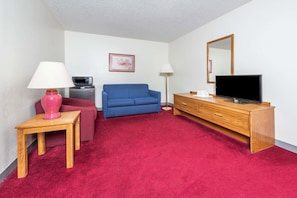A small room with a red carpet, a blue sofa, a wooden dresser, a television, and a microwave. - Super 8 by Wyndham Front Royal Near Shenandoah National Park (Front Royal)