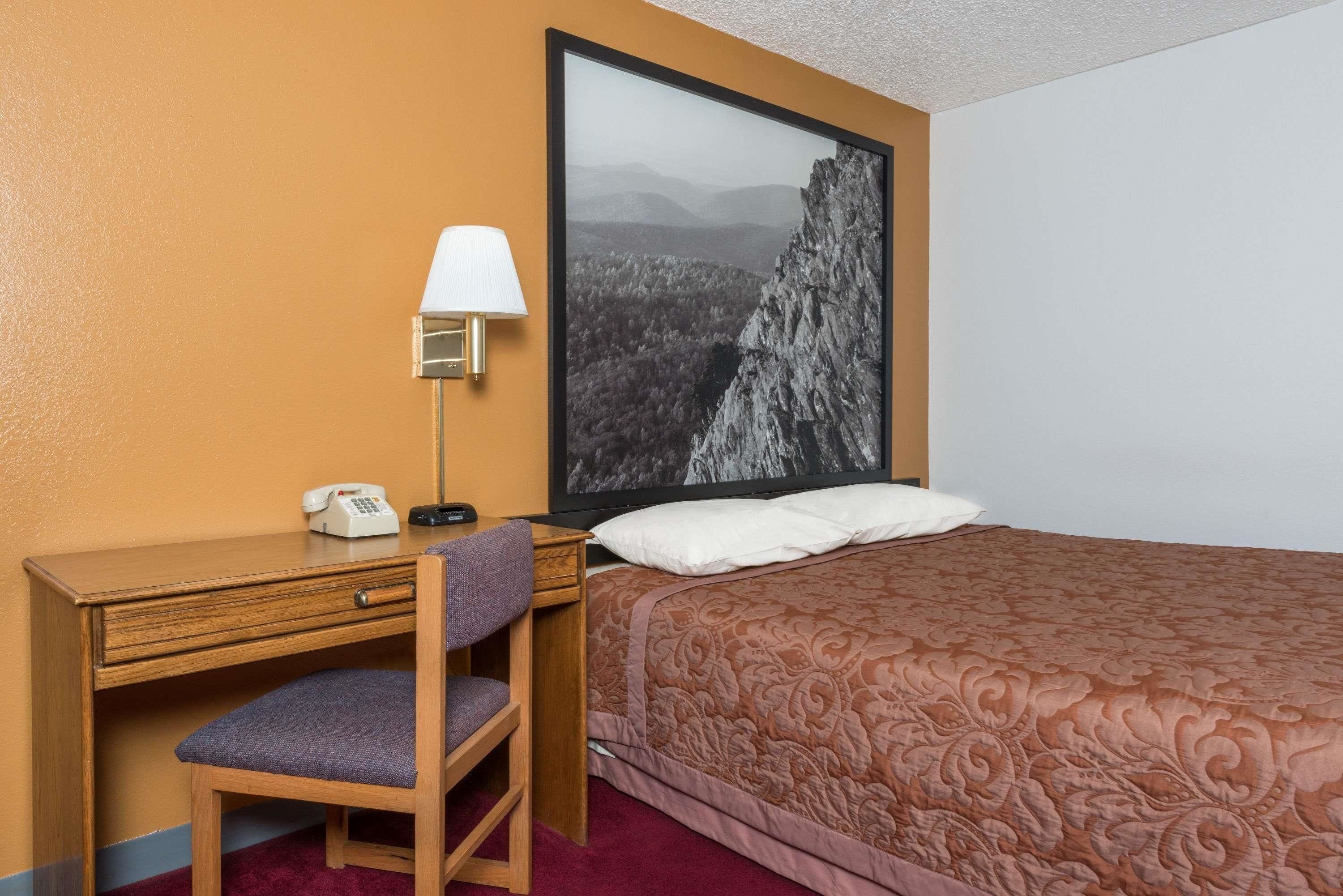 Een hotelkamer met een bed, een bureau met stoel, een telefoon en een wandlamp.