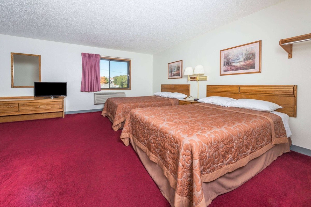 Quarto de hotel com duas camas, televisão, janela com vista e obras de arte nas paredes.