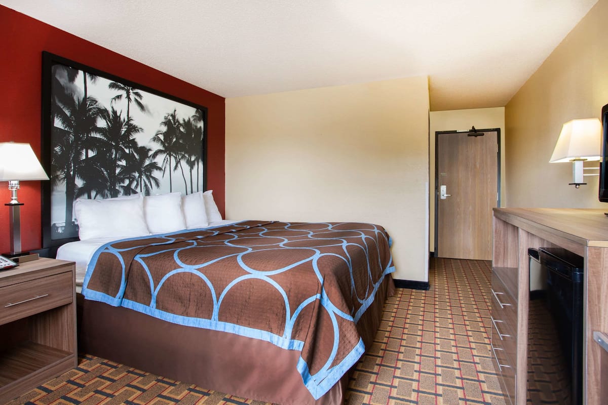 Une chambre d’hôtel comprenant un lit, une table de chevet, un bureau, une chaise, une porte et une lampe fixée au mur.