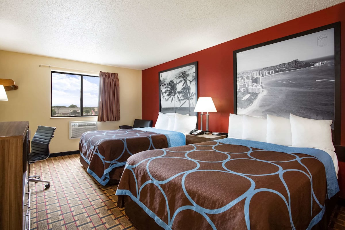 Une chambre d’hôtel avec deux lits, un bureau, une chaise et une grande fenêtre.