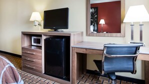 Een hotelkamer met een bureau, een stoel, een televisie, een koelkast, een magnetron en twee lampen.
