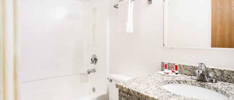 A bathroom with a white toilet, a shower, a sink with a granite countertop, and a mirror.