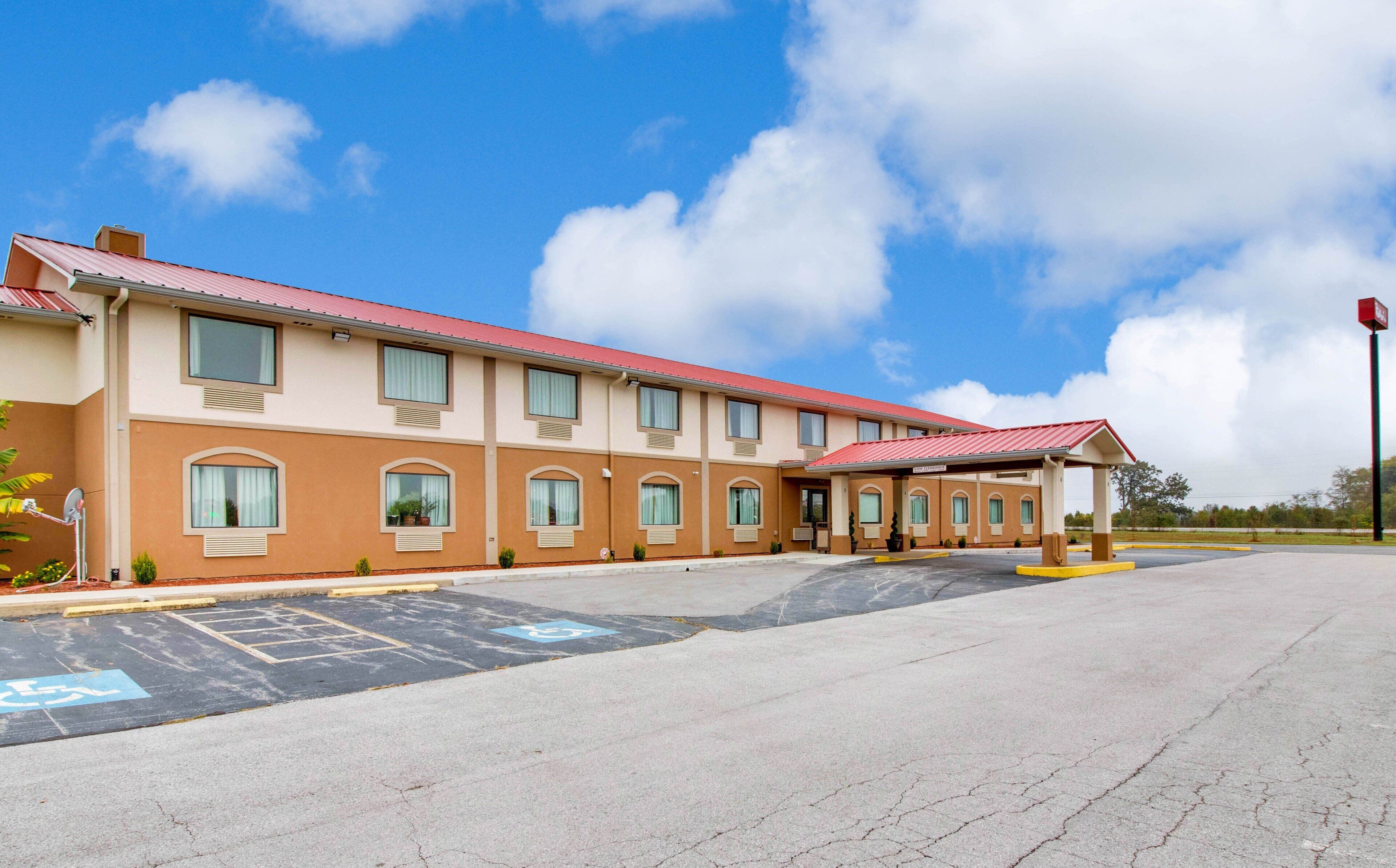 A multi-story hotel with a red roof, parking lot, and a covered entrance.