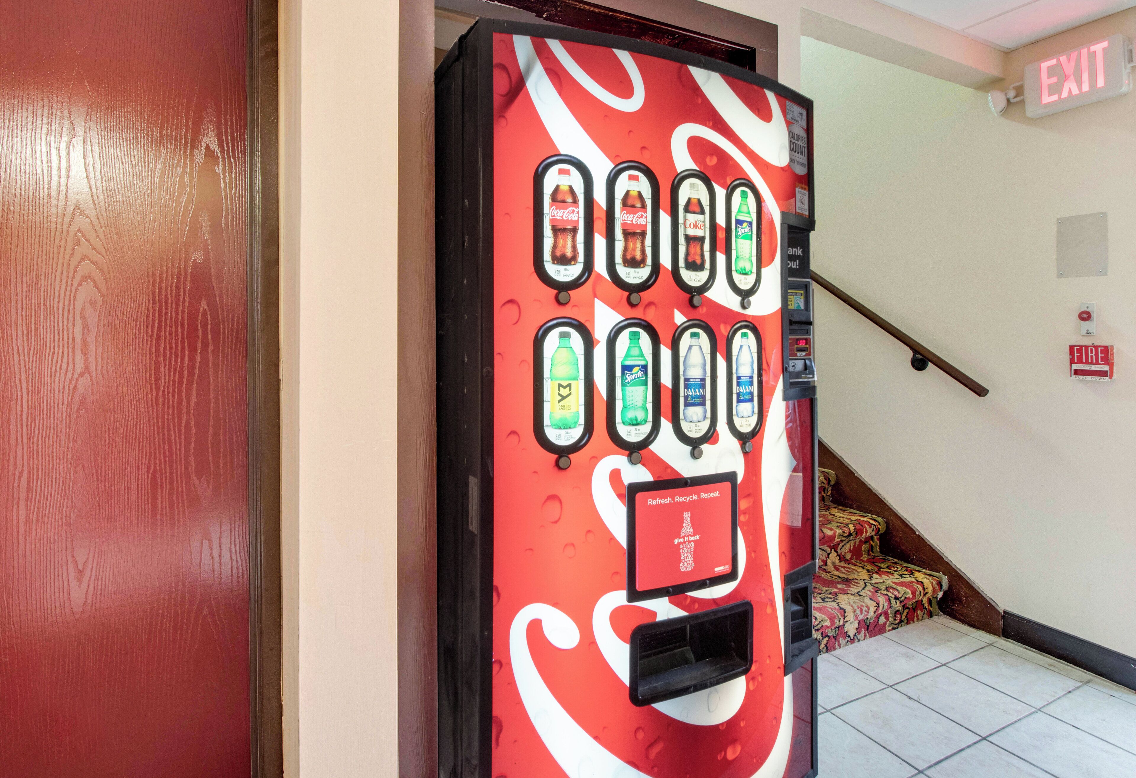 A vending machine with various drink options, an exit sign, and a fire alarm.
