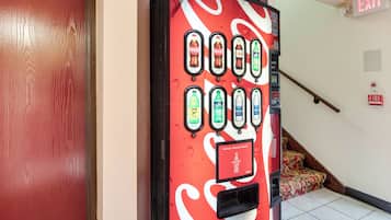A vending machine with various drink options, an exit sign, and a fire alarm.