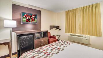 Une chambre d’hôtel avec un lit, un bureau doté d’un micro-ondes, une chaise rouge, un téléviseur fixé au mur et une fenêtre avec des rideaux.