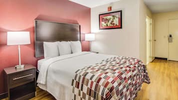 A hotel room with a bed, nightstands, a wall-mounted lamp, a framed picture, and a door.