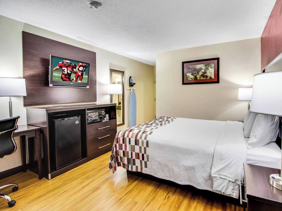 A hotel room with a bed, a desk, a television, and a painting on the wall.